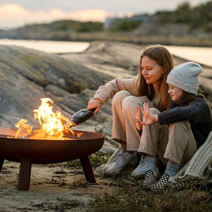 Two people warming up beside a portable firepit at the shore