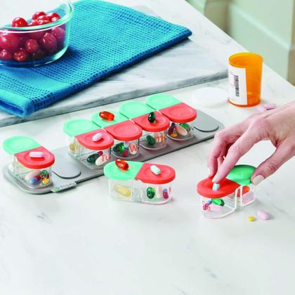Hands pressing open the lids of a weekly pill organizer